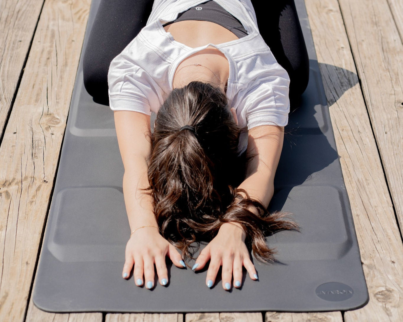 Person lying on a yoga mat outdoors on a wooden deck